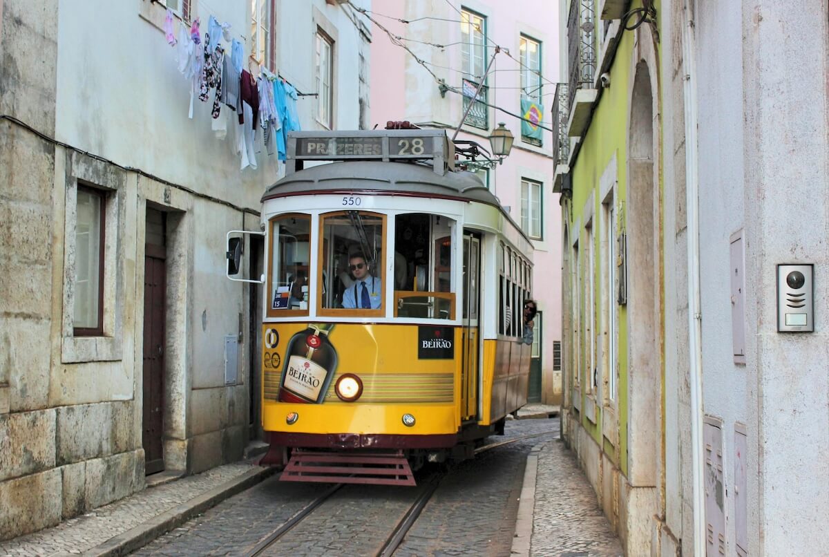 Historic yellow tram navigating a narrow Lisbon street with traditional architecture