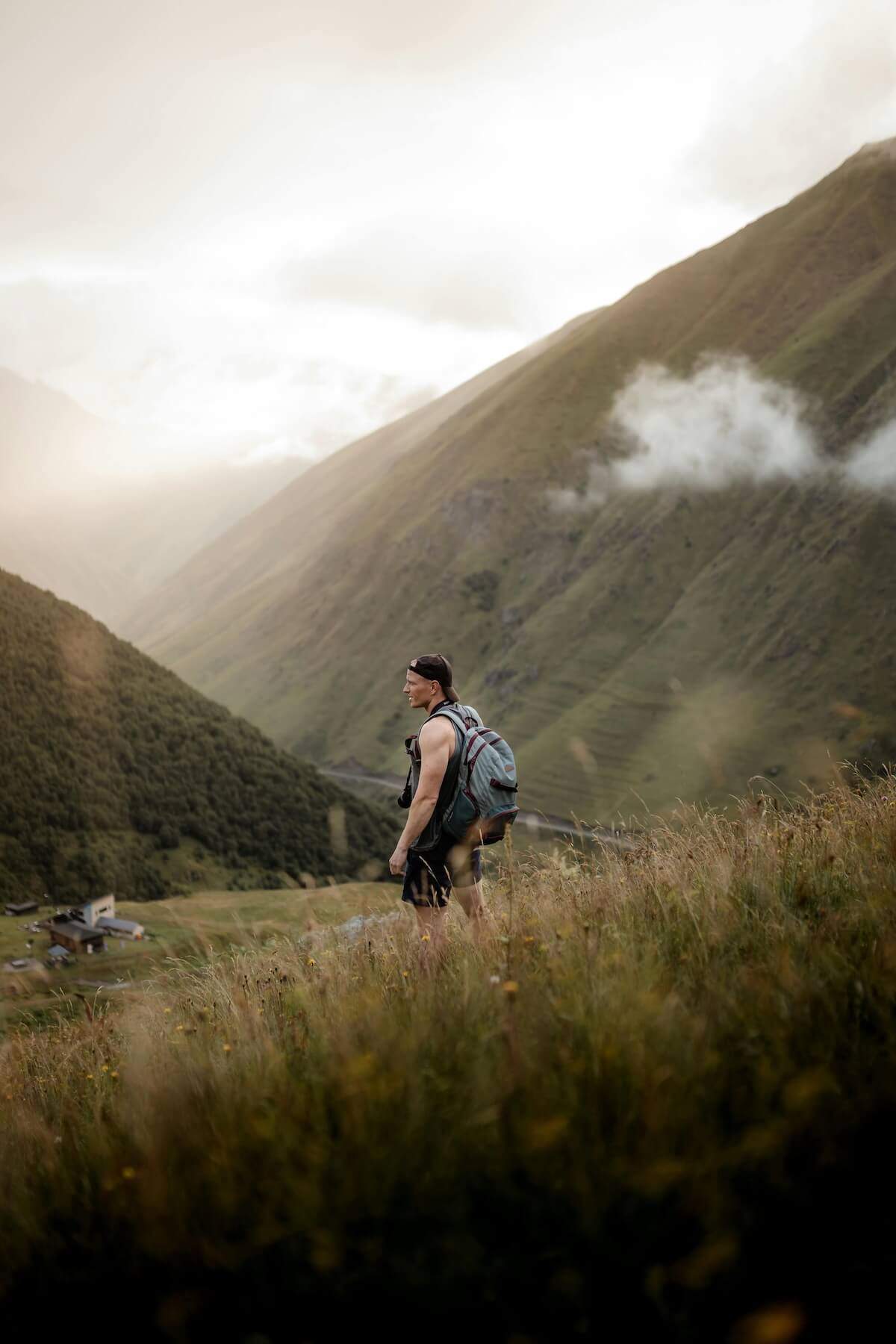 Solo hiker with backpack traversing grassy mountain hills in misty landscape