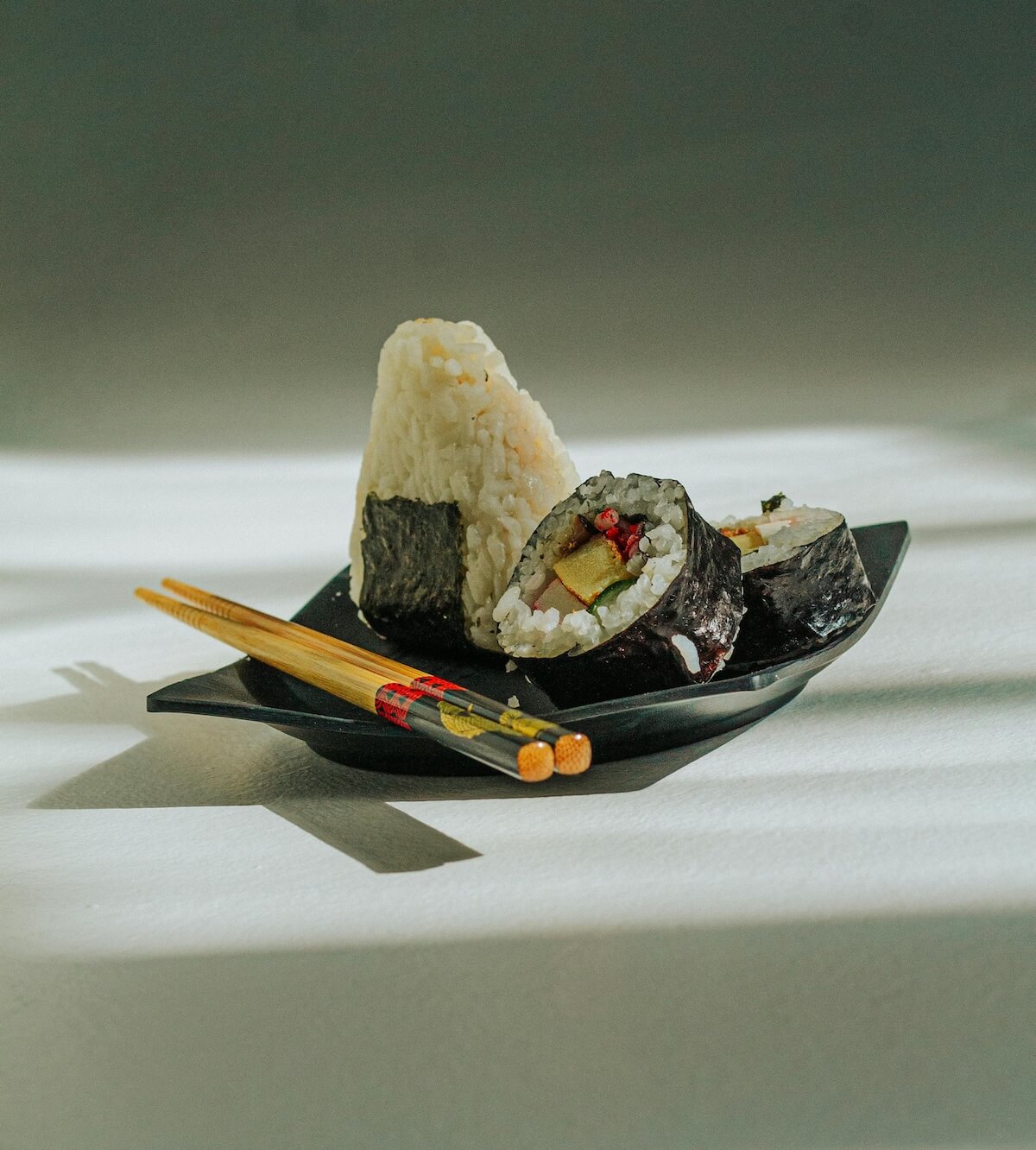 Japanese sushi rolls and onigiri rice balls with chopsticks on plate showing konbini food