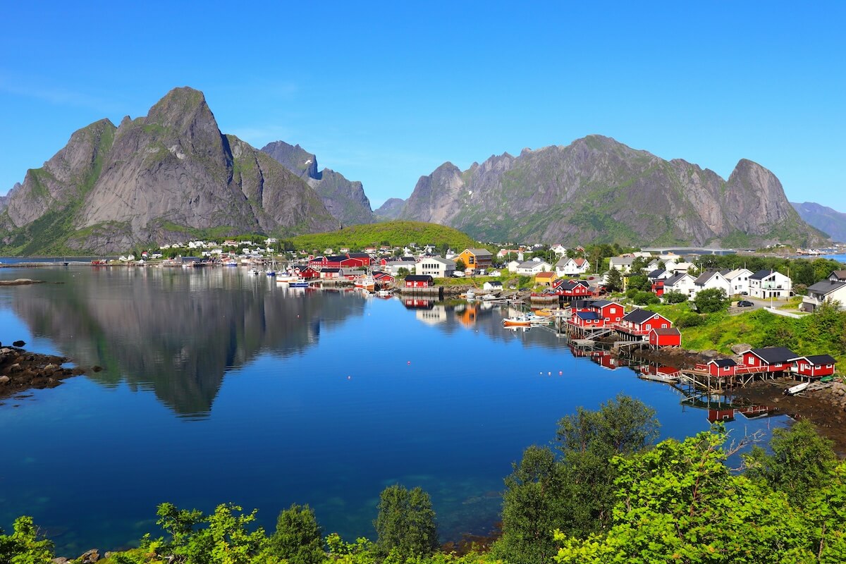 Reine village in Lofoten with red cabins and dramatic mountain backdrop reflected in calm water