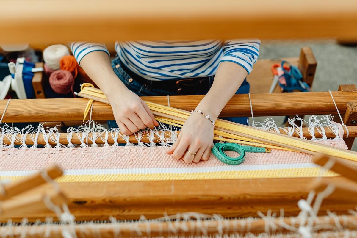 Hands working on traditional weaving loom with colorful threads, showing textile craftsmanship