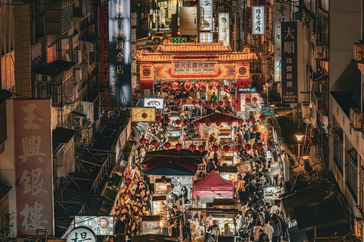 Bustling Raohe Street Night Market in Taipei with illuminated food stalls and crowds