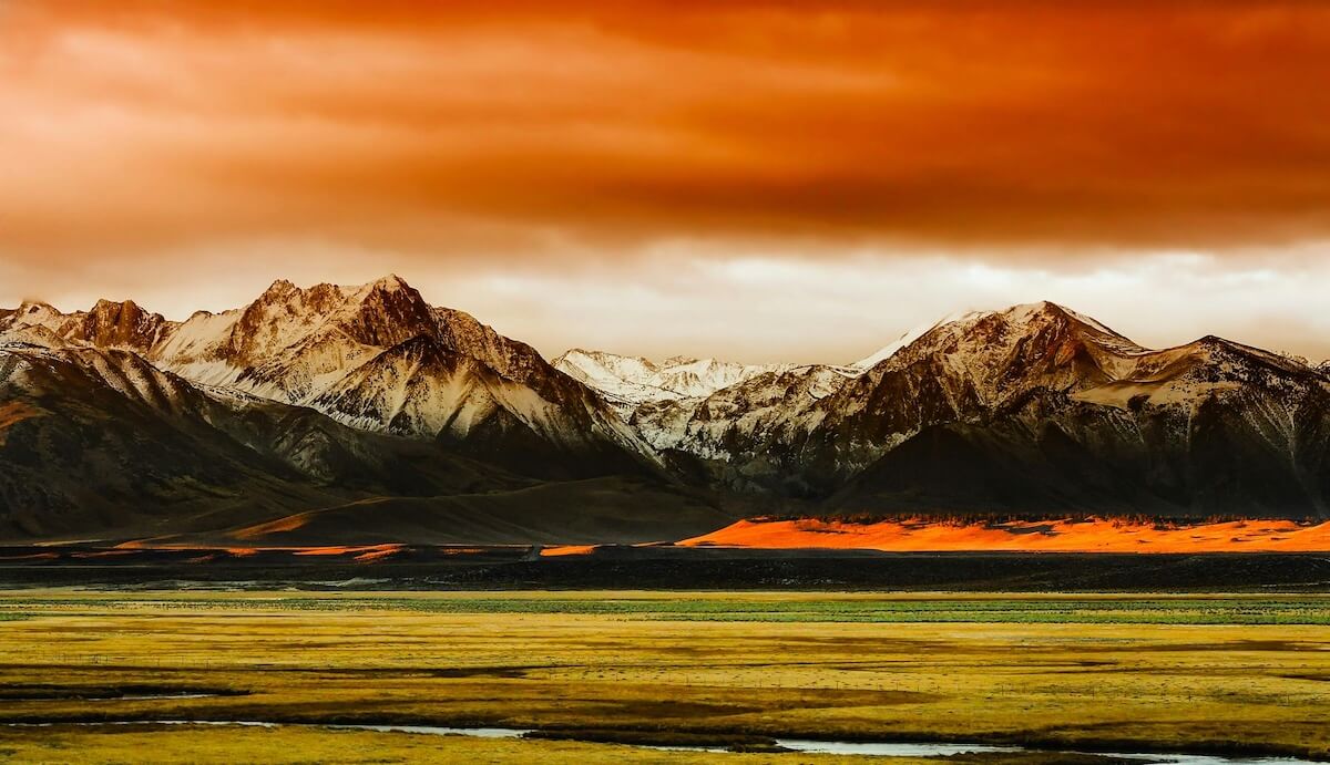 Snow-capped mountain peaks under a vibrant orange sky at sunset
