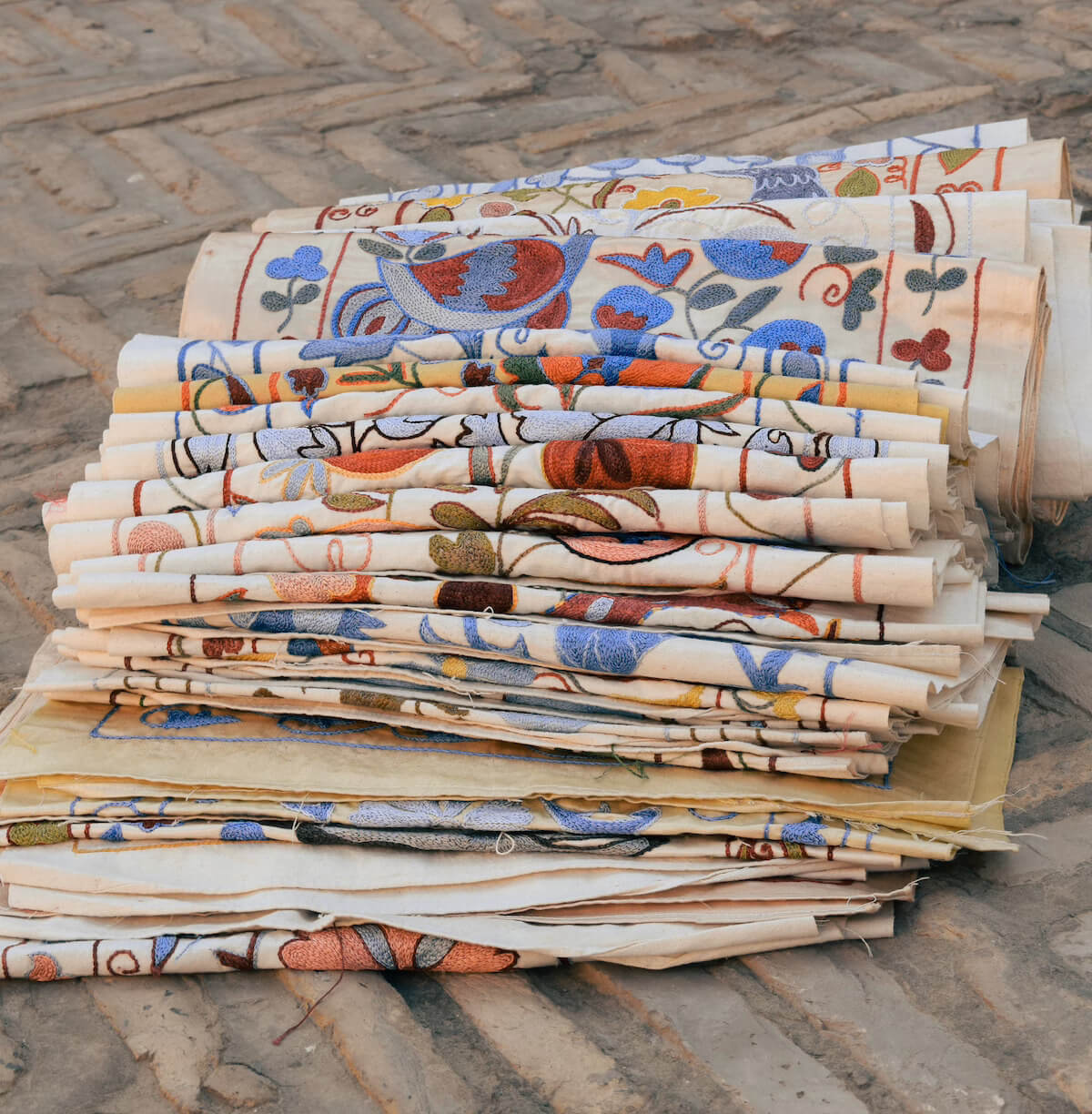 Stacks of brightly coloured embroidered textiles displayed on a stone ledge in Khiva, Uzbekistan