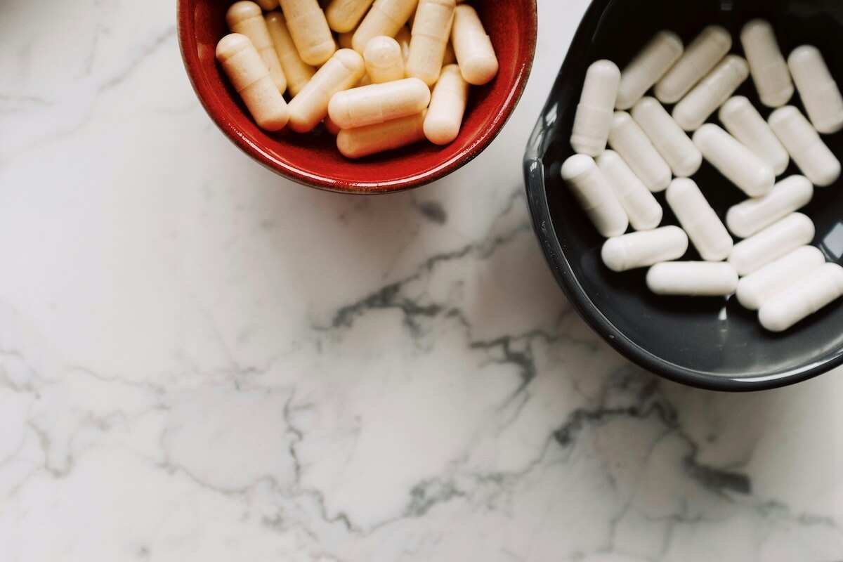 Assorted medication capsules and pills in bowl on marble surface