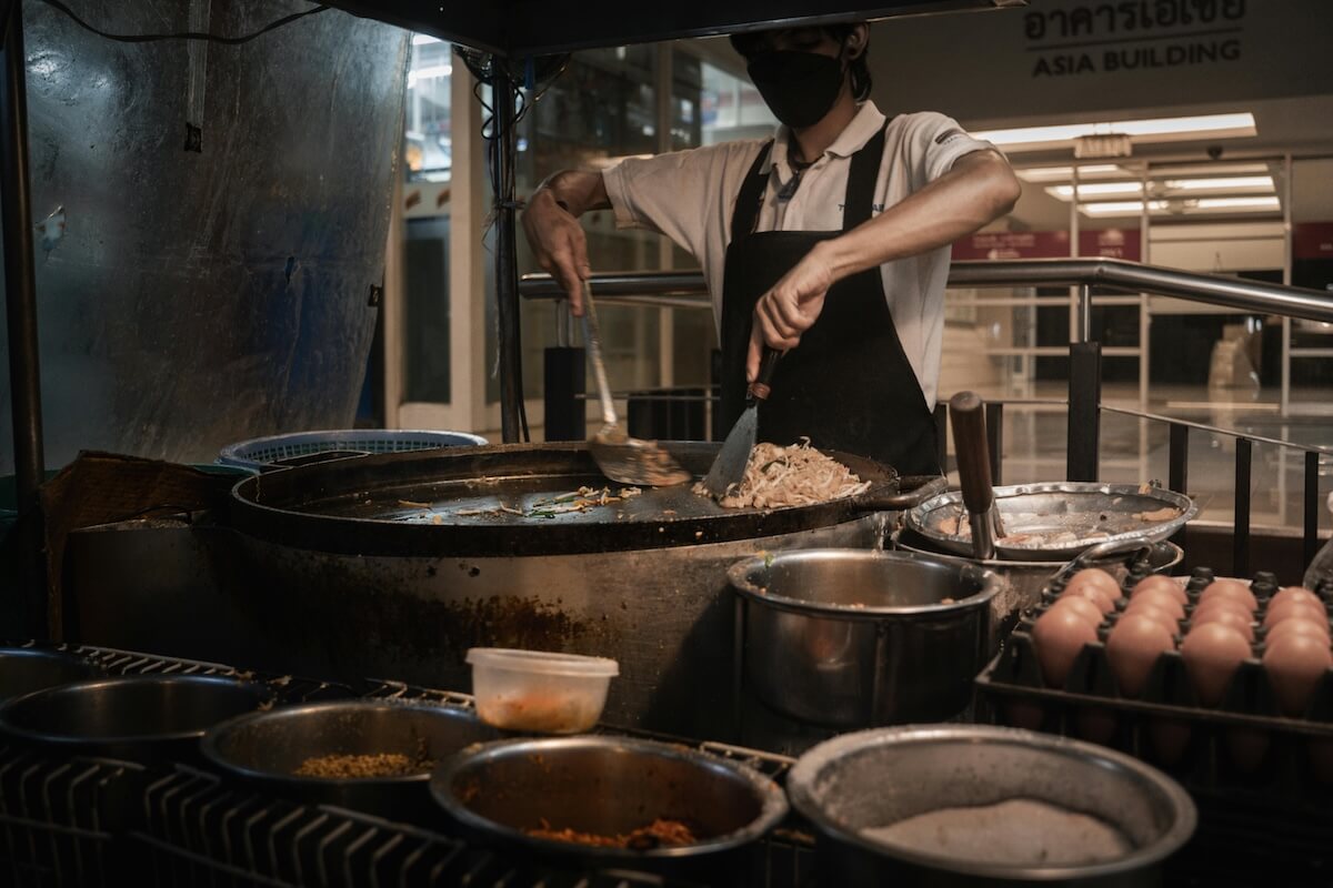 Chef cooking noodles at a Bangkok night market stall over an open flame
